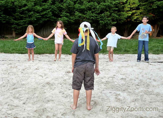 Children are seen in the background holding hands. One child has their back to the camera facing the other children in this example of tag games